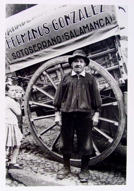 A man stands in front of a large wooden cart with a sign that reads 